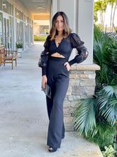 Load image into Gallery viewer, Black jumpsuit features a pom pom trim along with the neckline and cutout detail at the center front.
