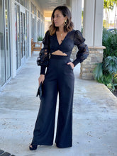 Load image into Gallery viewer, Black jumpsuit features a pom pom trim along with the neckline and cutout detail at the center front.
